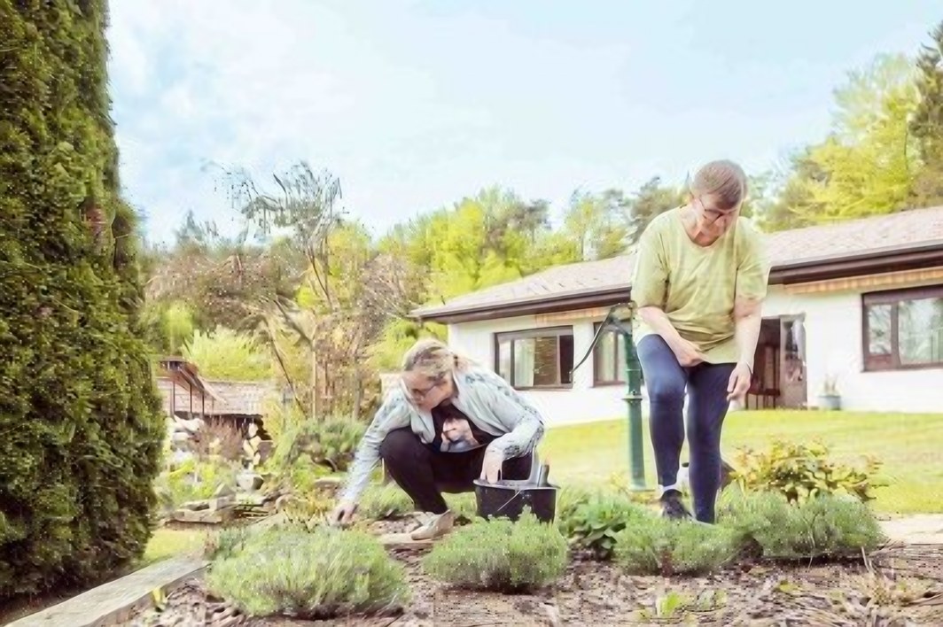 Zwei Personen pflegen ein Blumenbeet vor dem Haus