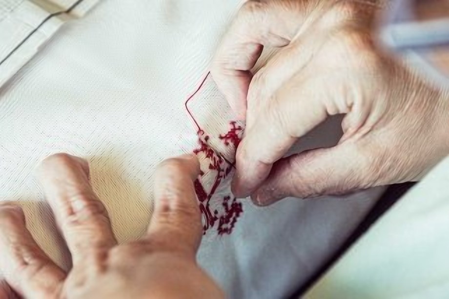 Hände sticken ein feines Perlenmuster auf Stoff