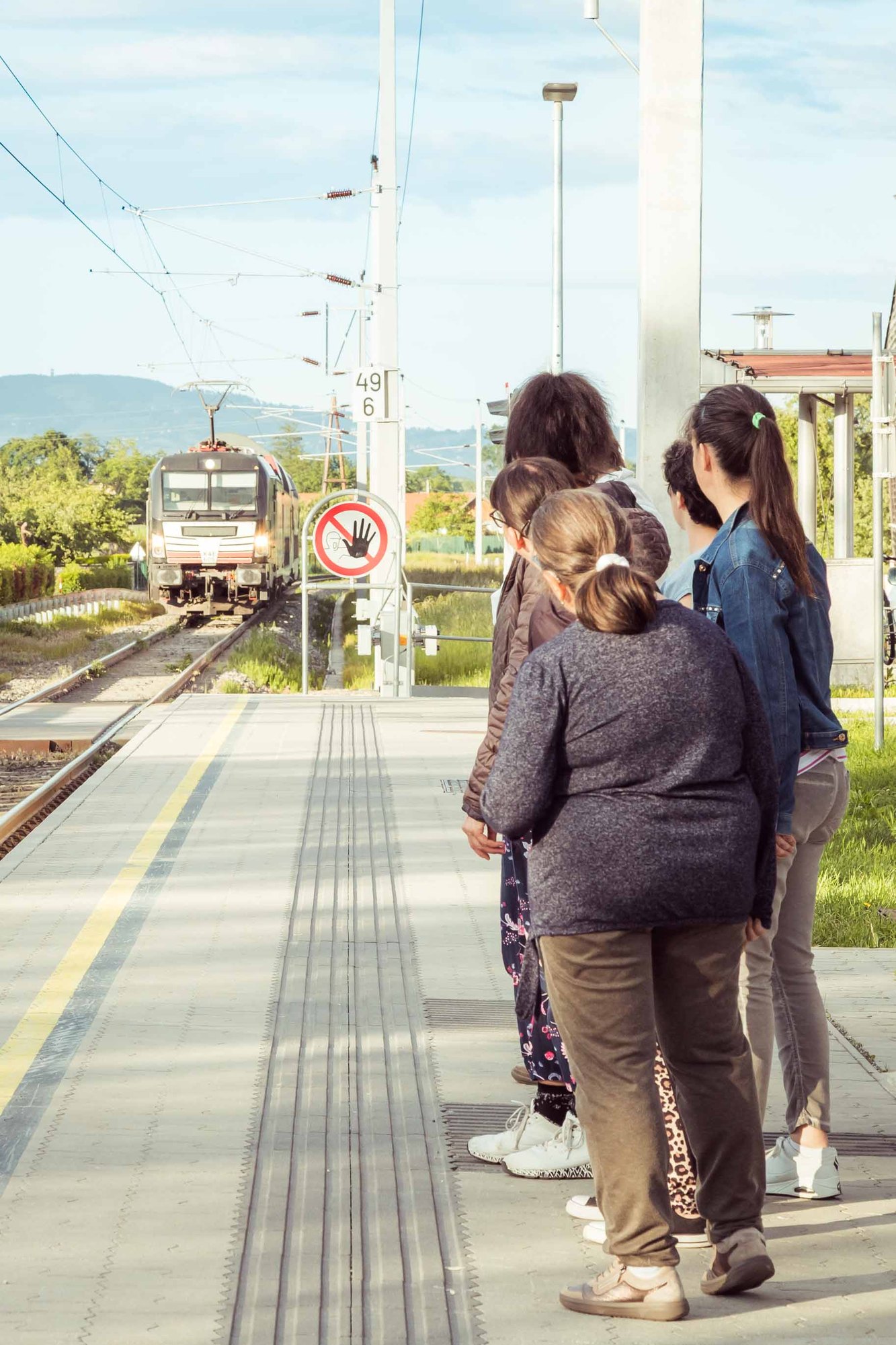 Eine Gruppe wartet am Bahnsteig auf den einfahrenden Zug